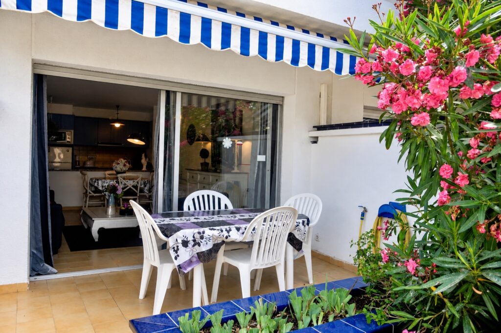 Terrasse couverte avec table, store rayé et laurier-rose — appartement Dalí, La Fosca Bay (Palamós, Costa Brava)